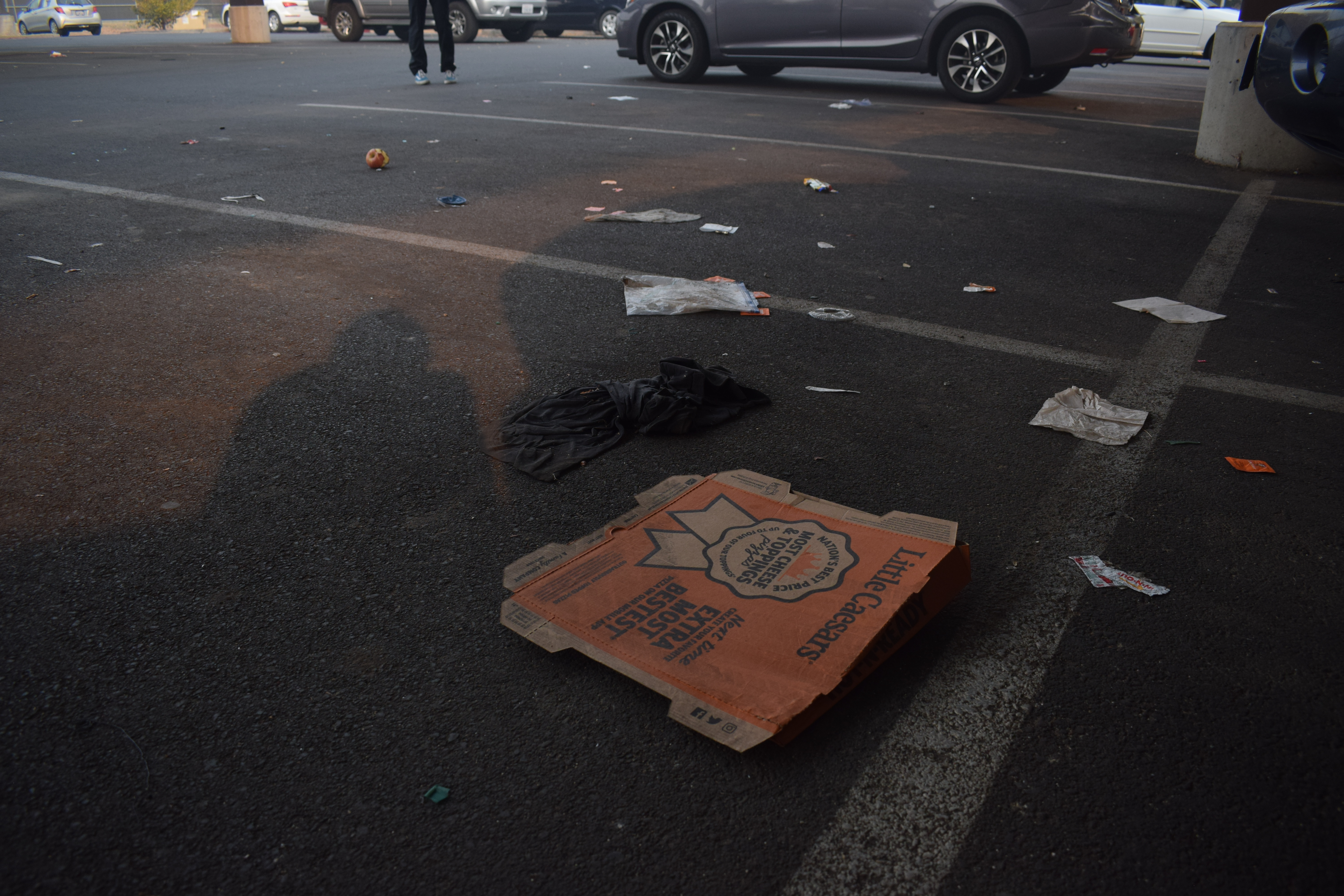 A run-over Little Caesars Pizza box rests in the middle of the parking lot.
