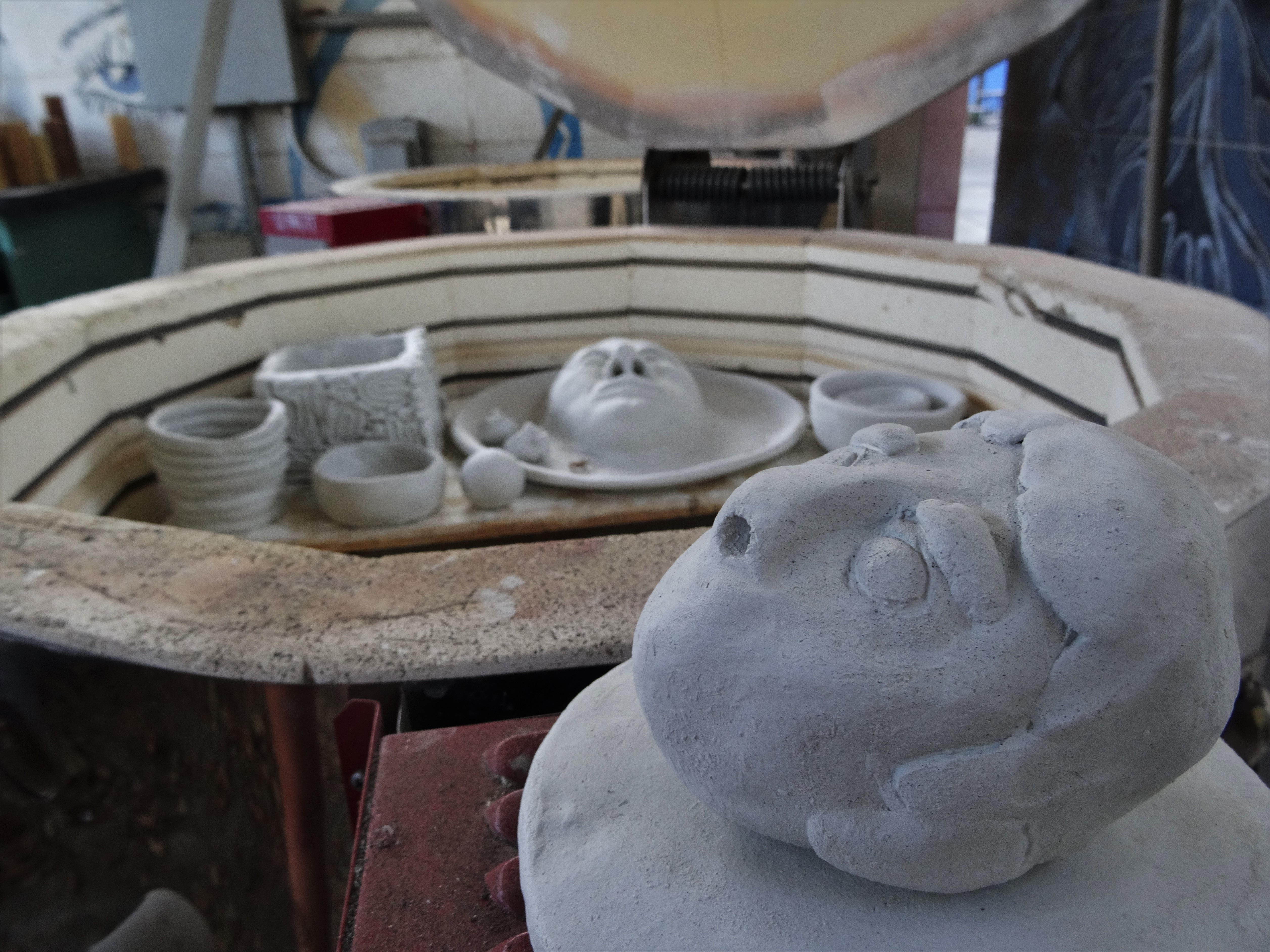 A sculpture that looks like a face sits next to a kiln full of other clay projects.