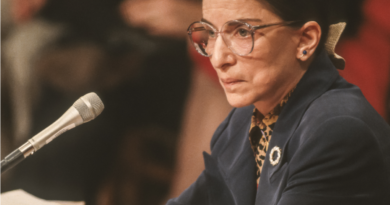 Justice Ruth Bader Ginsburg sitting with arms crossed in front of a microphone
