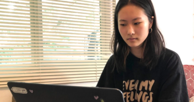 Senior Anne Zhao sitting on her bed with hands on her open laptop in front of her navigating the Canvas homepage