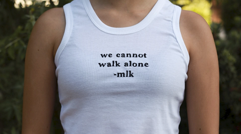 A student wearing a white tank top reading "we cannot walk along -mlk"