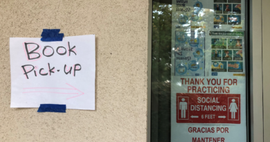 A paper sign reading "Book Pick-up" with an arrow to the right taped on the wall next to a classroom window