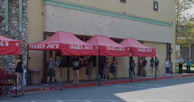 A line of people waiting around a building under red tents labeled "Trader Joe's"