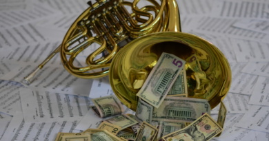 Money spilling out of a French horn on top of scattered music sheets