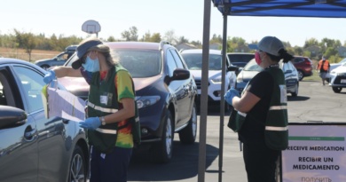 A volunteer dispenser checking a patient's paperwork in front of a line of cars