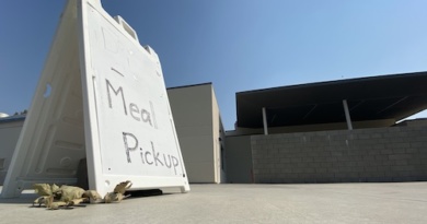 A sign that reads "Meal Pickup" sits in front of the All Student Center. The sign is located on the backside of the All Student Center or the Davis High cafeteria where nutrition staff are serving lunches.