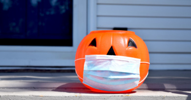 A plastic jack o' lantern sitting on a front porch with a blue face mask