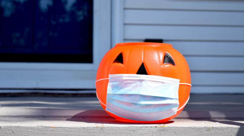 A plastic jack o' lantern sitting on a front porch with a blue face mask