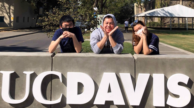 Three UC Davis students lean on a UCD sign