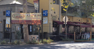 A huge "Open" sign in front of Crepeville in Downtown Davis directs customers to the business's website for online orders and take-out options