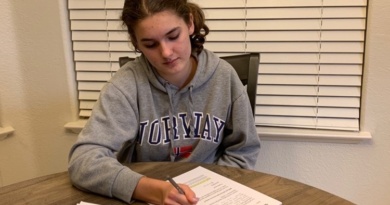 Senior Emma Carney is sitting at a table in her house writing a letter for Vote Forward.