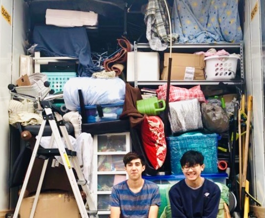 George Zhou and his friend Caleb Davis sit in the bottom right corner of Zhou's open moving van with all his belongings behind them