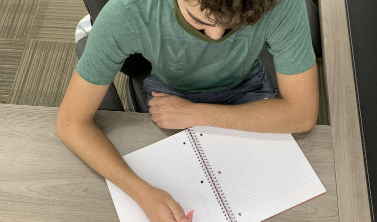Davis High alumnus Robbie Silver holding a pencil above his notebook, preparing to take notes for his online class.