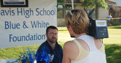 Will Arnold being interviewed by a person holding a camera. The sign behind him reads "Davis High School Blue & White Foundation"
