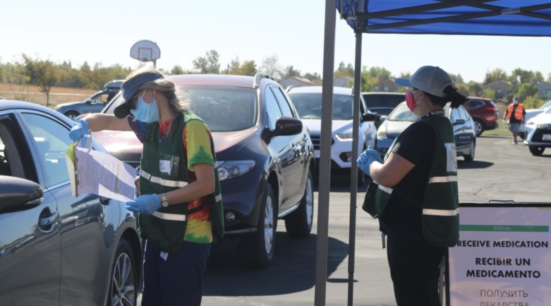 A volunteer dispenser checking a patient's paperwork in front of a line of cars