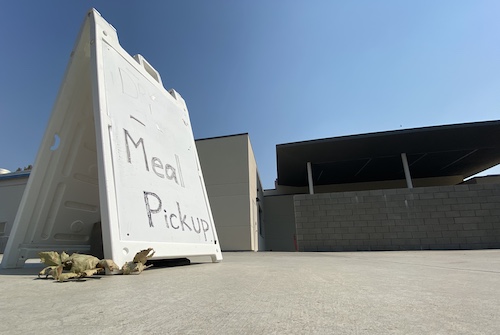A sign that reads "Meal Pickup" sits in front of the All Student Center. The sign is located on the backside of the All Student Center or the Davis High cafeteria where nutrition staff are serving lunches.